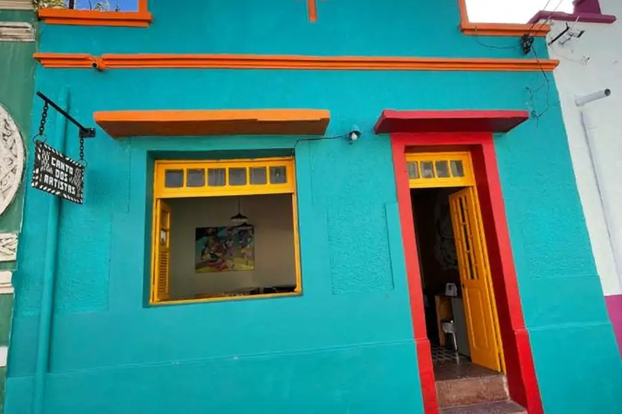 La façade turquoise, rouge et jaune de Hostel Canto dos Artistas avec son enseigne en bois, dans le Carmo, à Olinda
